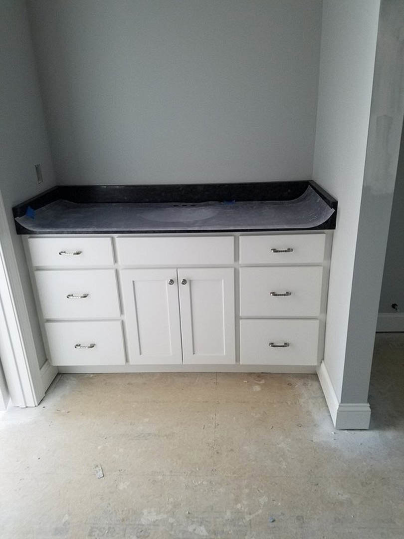 White kitchen cabinets with silver handles, light stone countertop, stainless steel sink, and smooth white flooring
