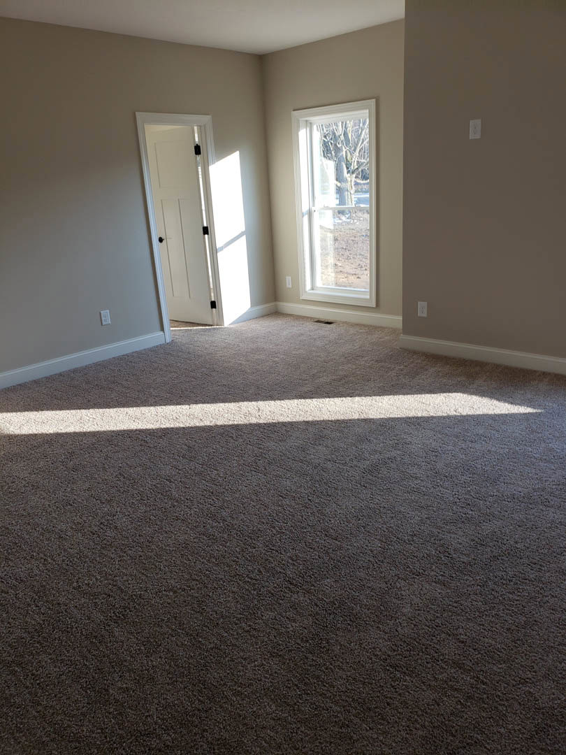 Carpeted room with white walls, white door featuring black knobs, window showing tree outside, light switch on wall