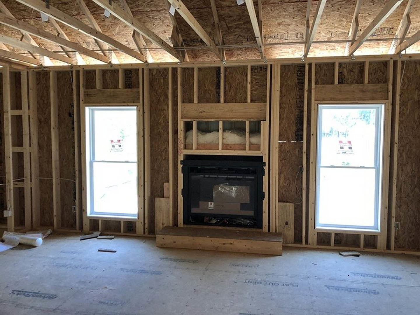 Living room with stone fireplace, large windows featuring sticker, exposed wooden ceiling beams, and hardwood floors.