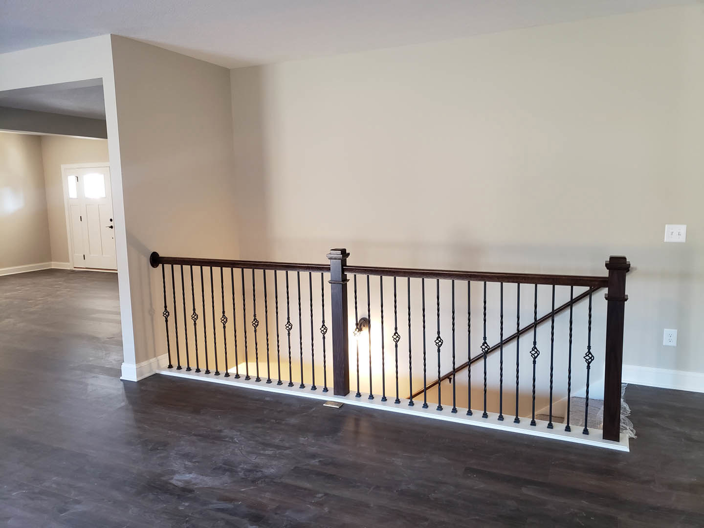 Wooden staircase with white balusters, hardwood floor, white door featuring three glass panes, wall sconce lighting, smooth plaster walls