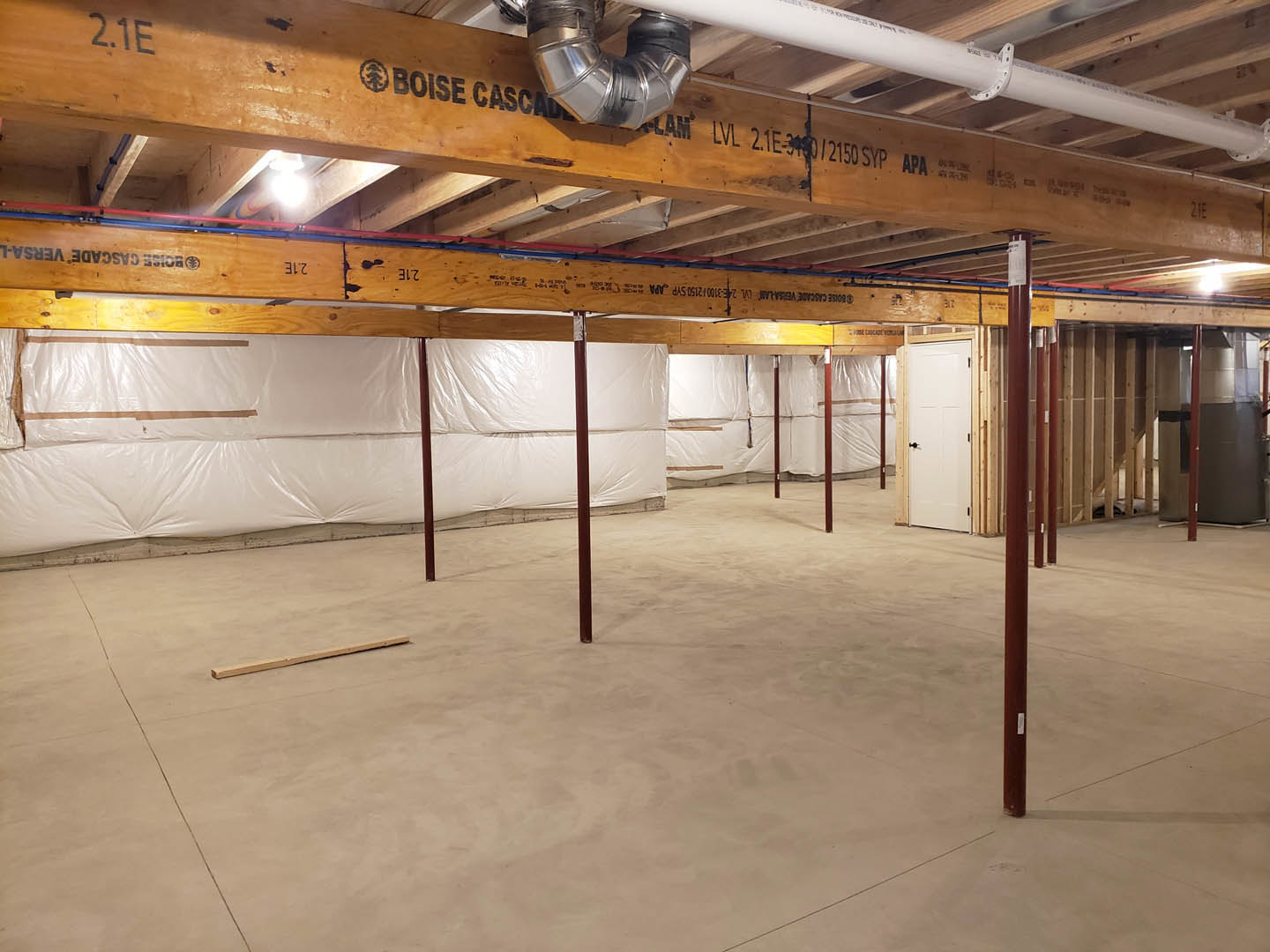 Exposed wooden ceiling beams, white walls, concrete floor with metal poles, white door featuring black handle, metal pipe attached to beam