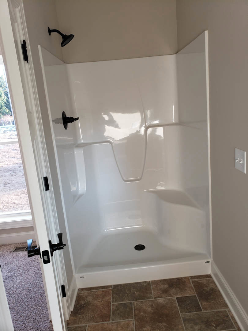 White tile shower with black hardware, black shower head mounted on white wall, tile floor visible in foreground