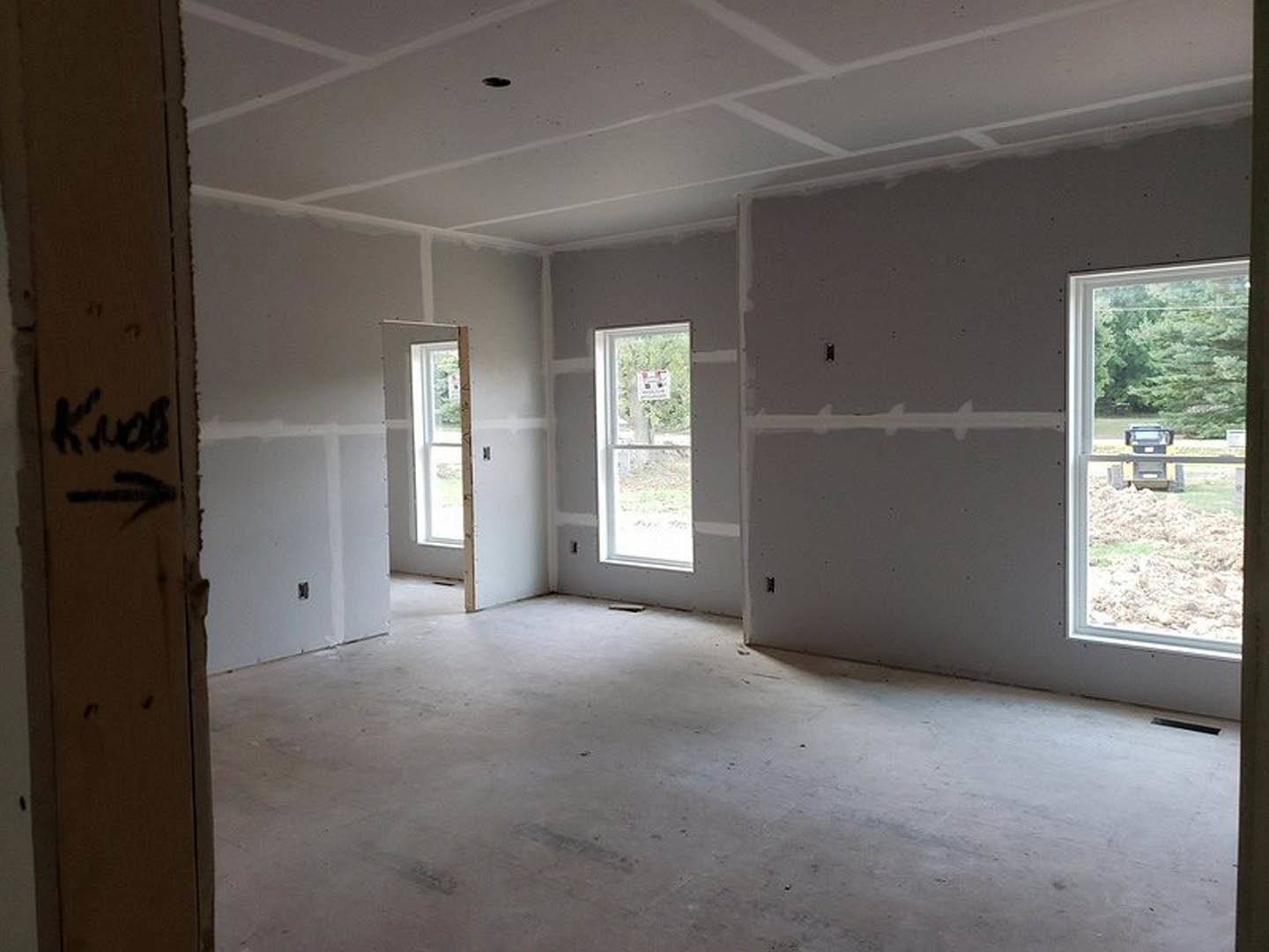 Spacious room with large windows, unfinished concrete floor, plaster walls, and construction site visible through window