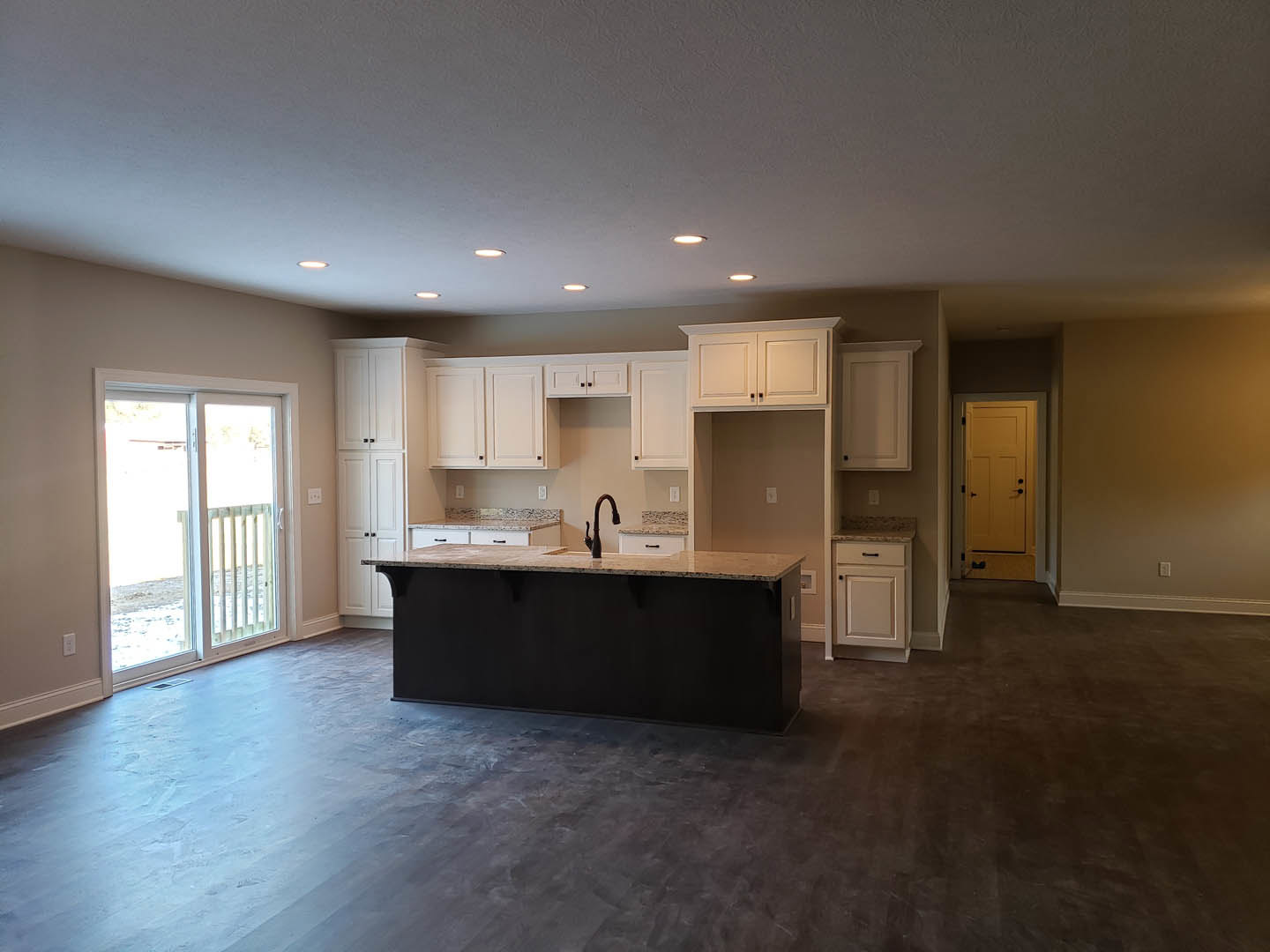 Kitchen with white cabinetry and black handles, black countertop island, large window, sliding glass door with white frame, yellow door with black handles, light wood flooring