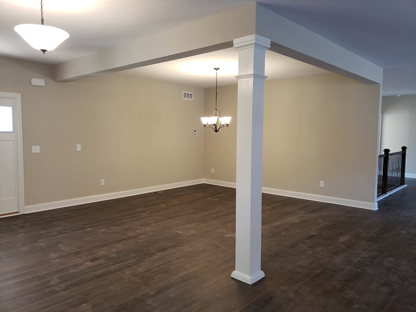 Wood flooring with a white column, white plaster walls, brown trim, and a ceiling light fixture.