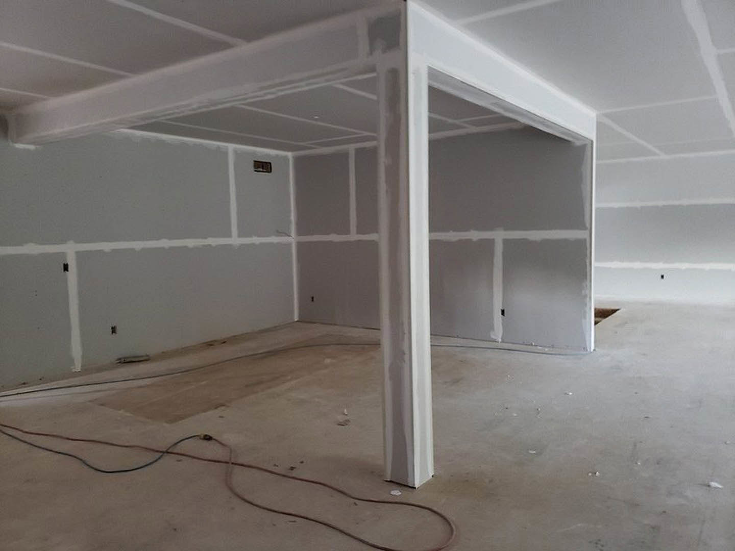 Empty room with white plaster walls and ceiling, white trim, grey flooring, loose wire on the floor, and a sheer white curtain