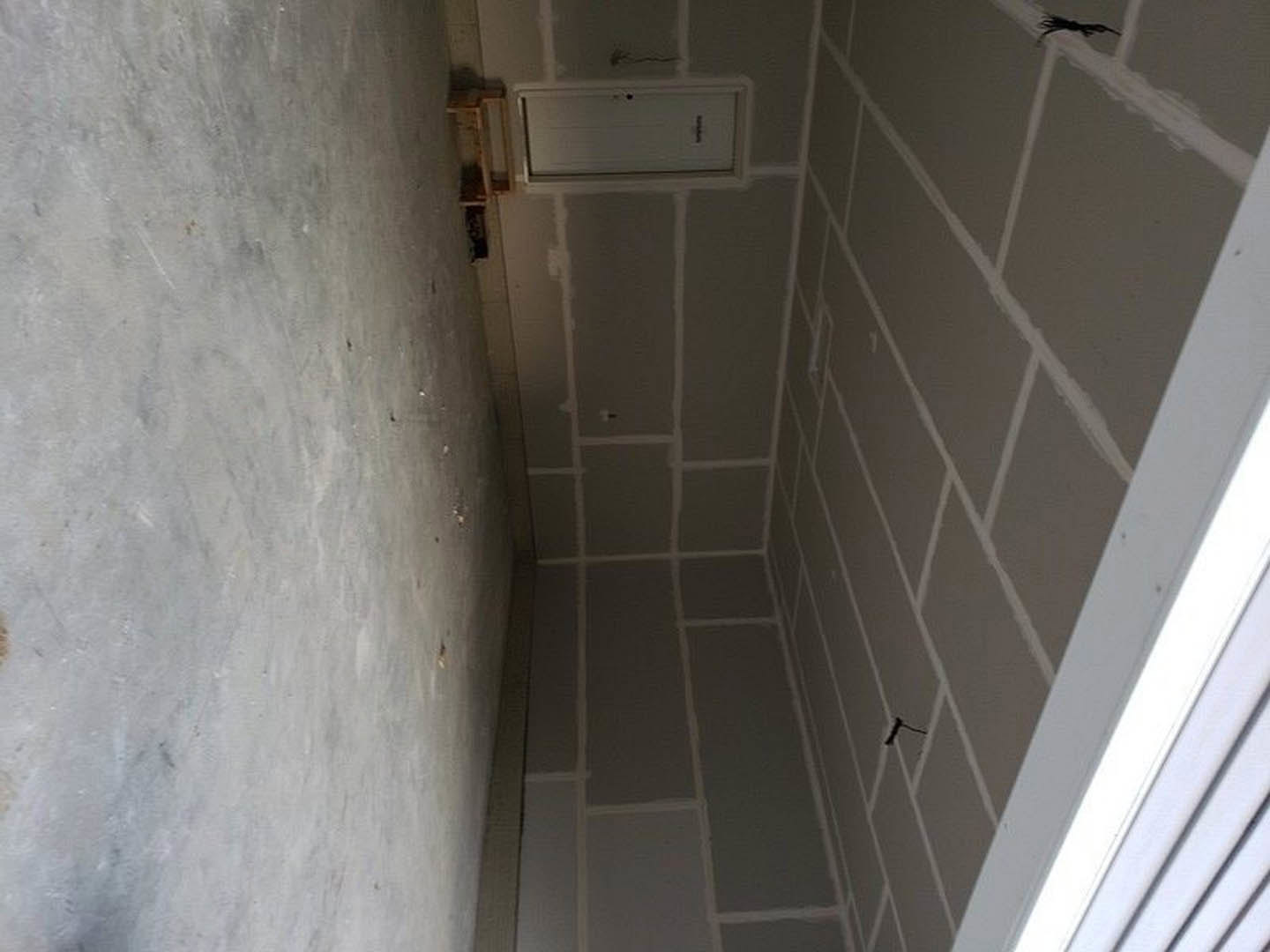 Bathroom with white plaster walls, grey tile flooring, glass shower enclosure, marble accents, and a black-framed door.
