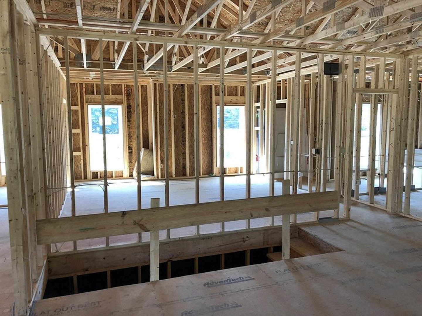 Wood-framed house under construction with exposed beams, unfinished walls, and daylight streaming through windows