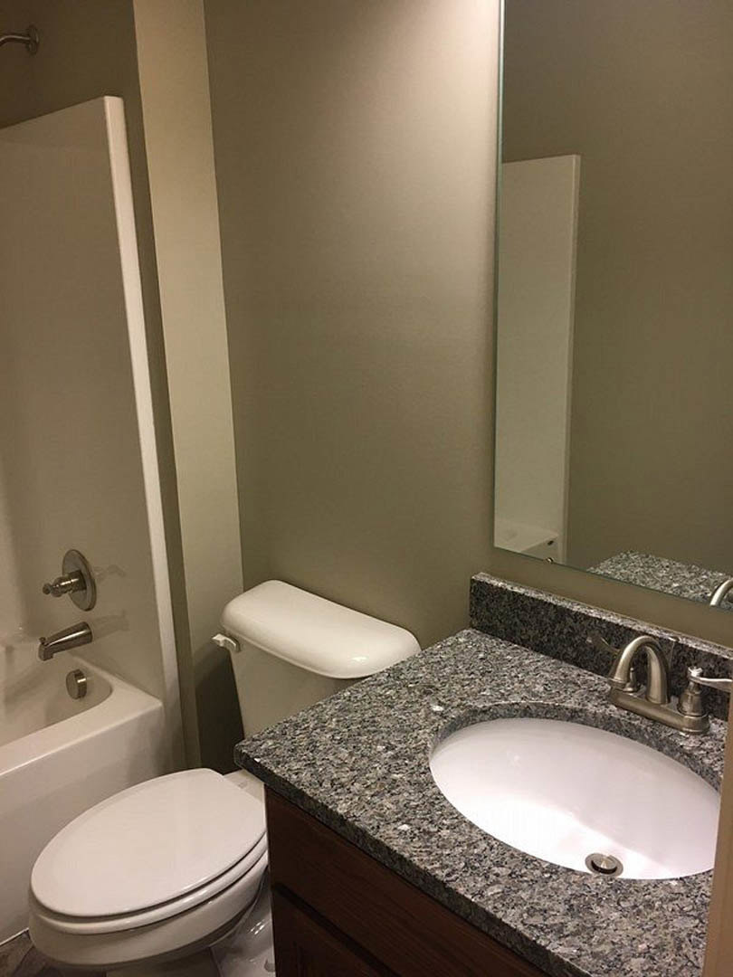 Bathroom with marble countertop vanity, undermount sink, chrome faucet, white toilet, tiled walls, and bathroom cabinet