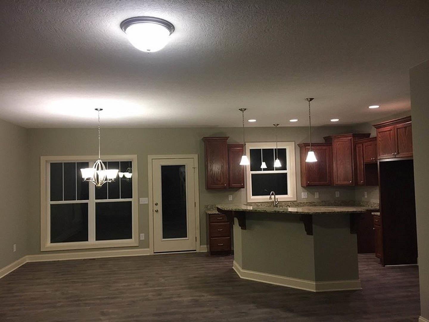 Open kitchen with white cabinetry, stone countertop bar, black and white door, modern ceiling light fixture, and white chandelier near a window