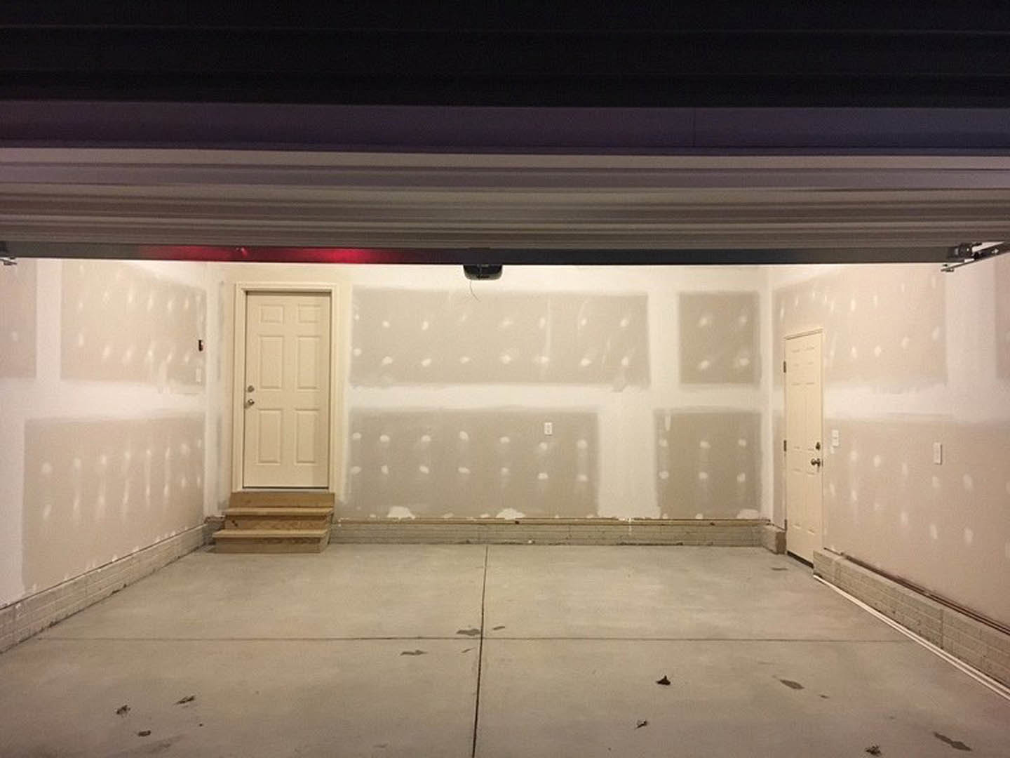 Garage interior with smooth white plaster walls, white entry door featuring a silver doorknob, exposed concrete floor, and ceiling.