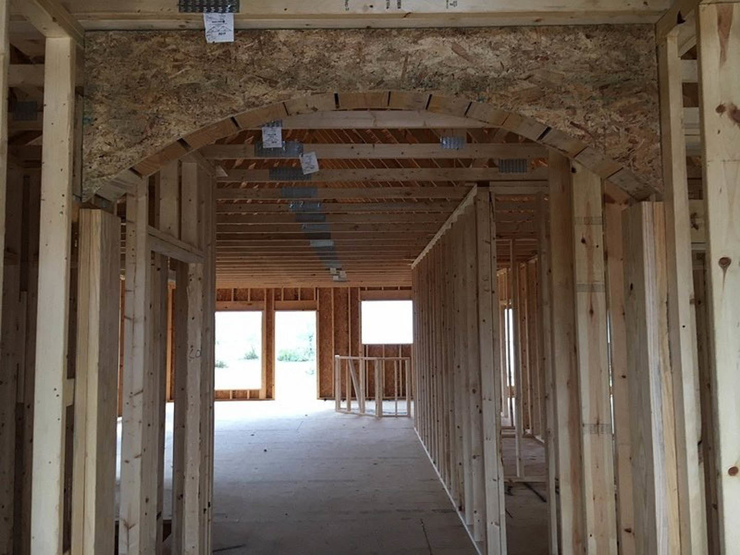 Exposed wood framing and beams inside a house under construction, concrete floor, metal railing, window frame, and white sign with black text