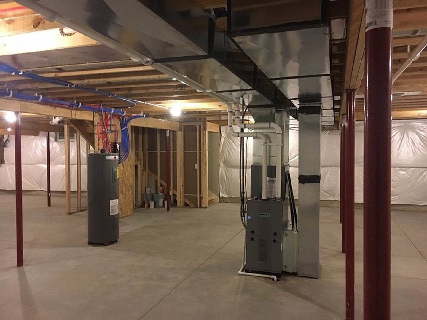 Utility room with exposed metal pipes, large grey mechanical unit, black cylinder with white label, grey electrical box, and computer equipment on the floor.