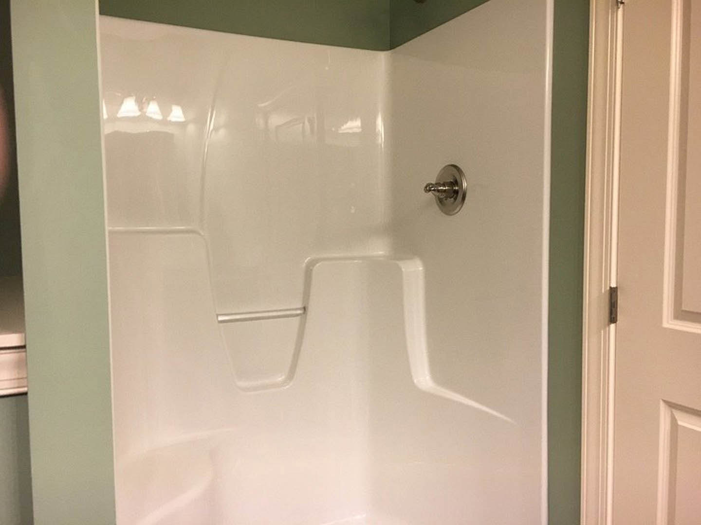 White tiled shower wall with a silver handle, close-up of a metal hook, and a door hinge on a white bathroom door