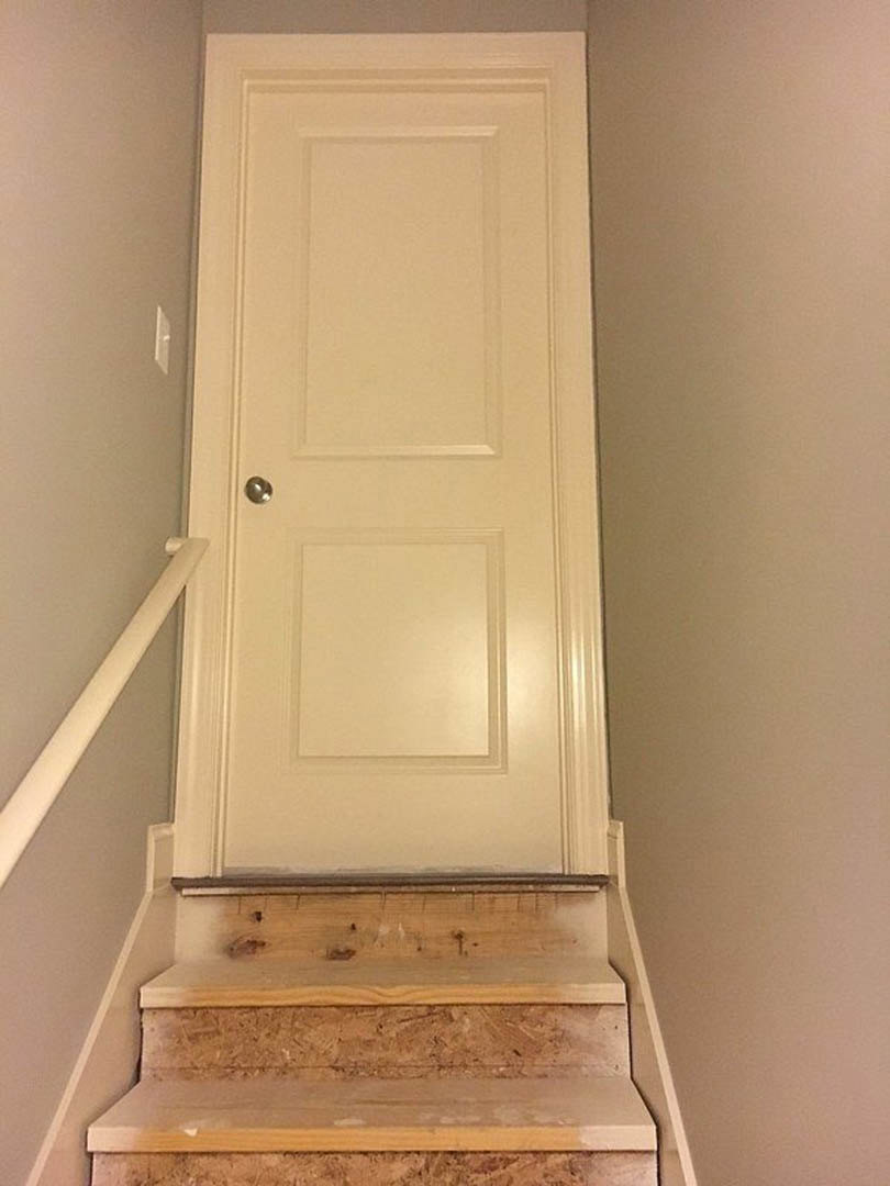 White interior door with silver handle beside wooden stairs and built-in wood shelf, white walls and base molding