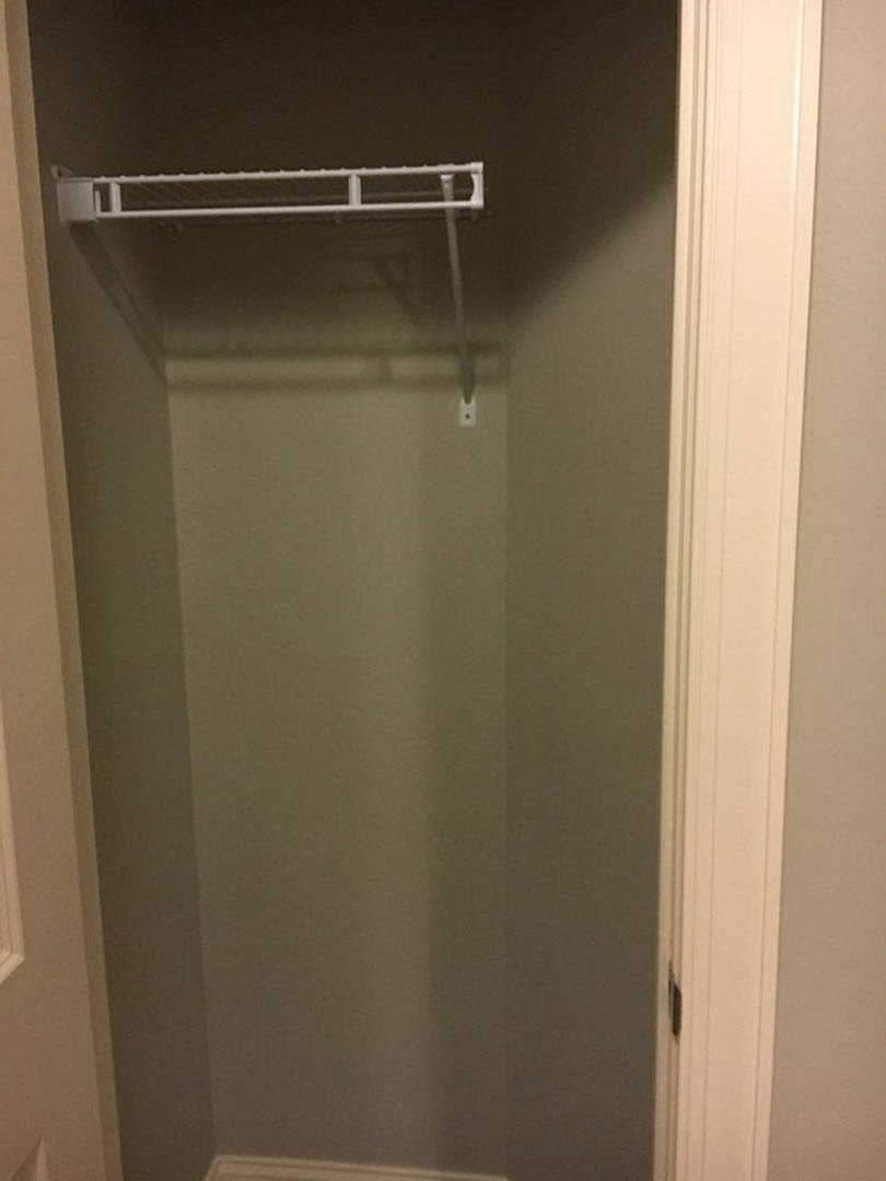 White closet with built-in shelf and metal hanging rod, black door handle on white door, smooth painted walls