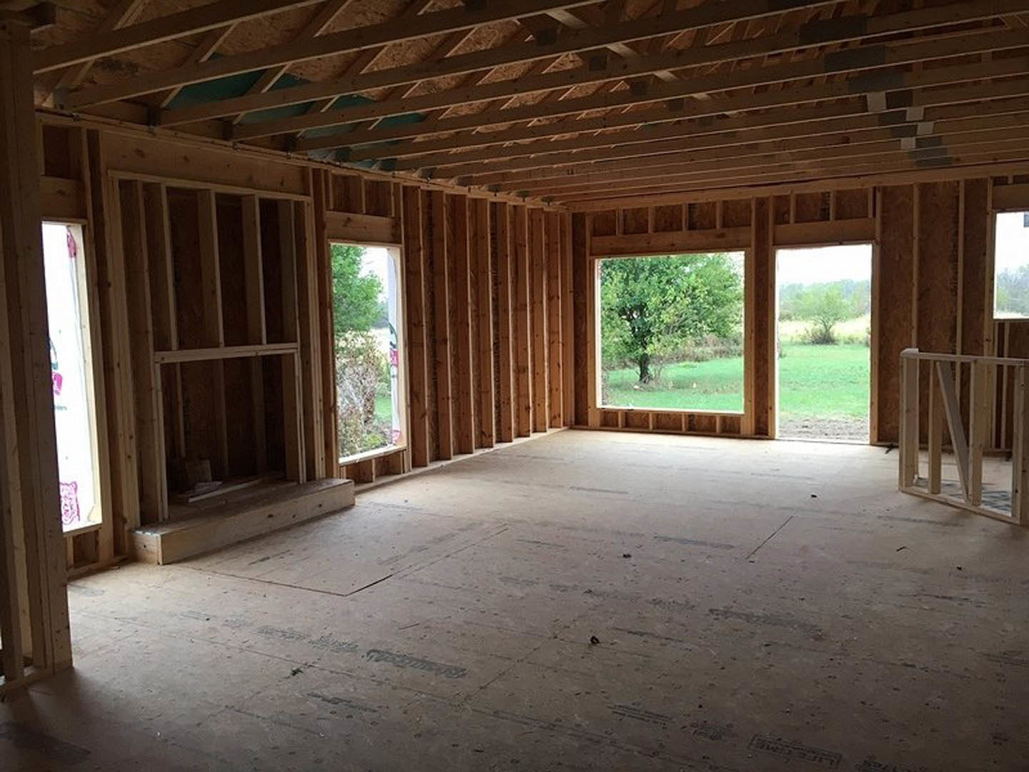 Exposed wood ceiling beams, large windows with tree views, light hardwood floors