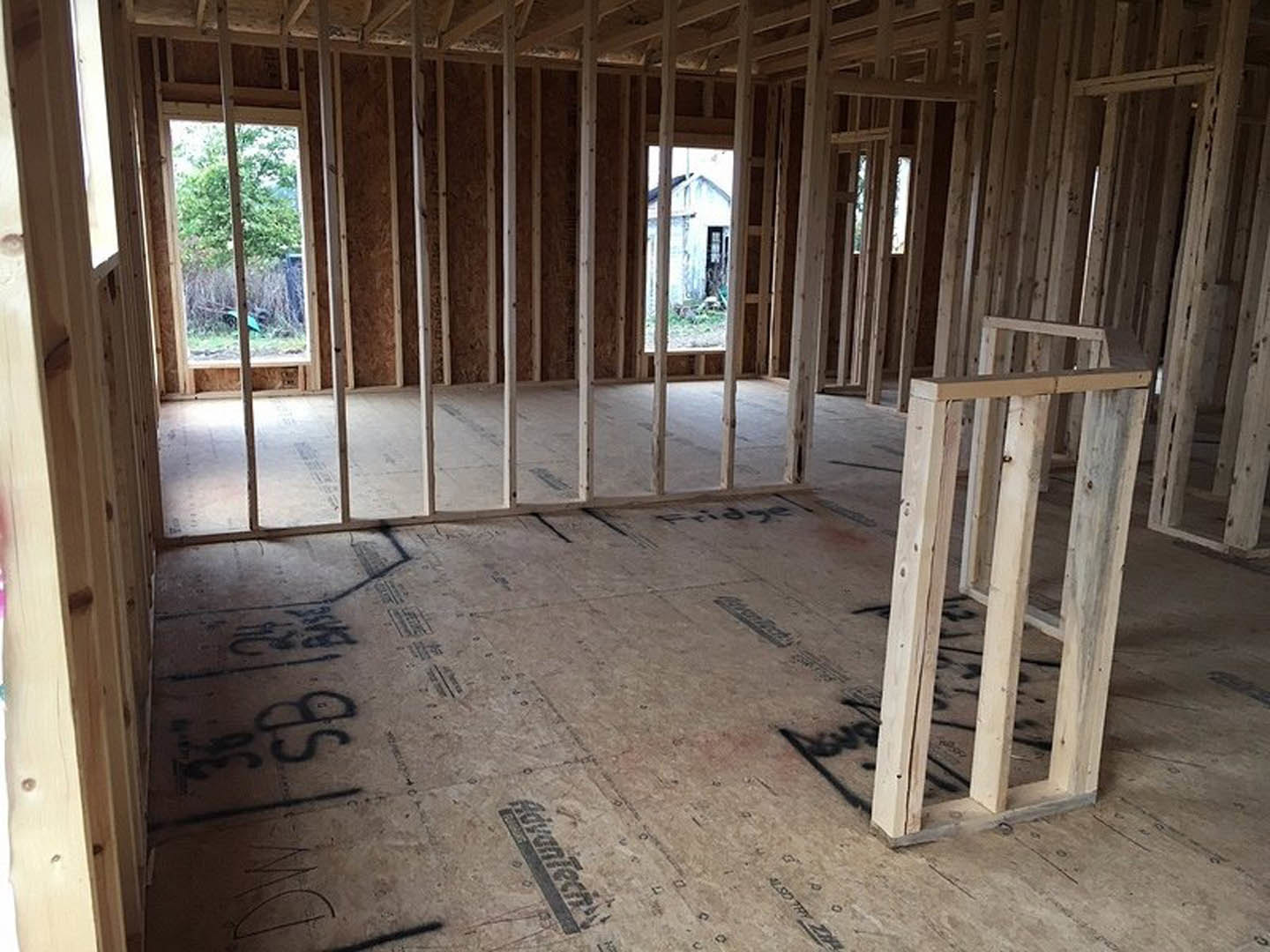 Room under construction with exposed wood framing, ceiling beams, unfinished floor, and a window overlooking trees