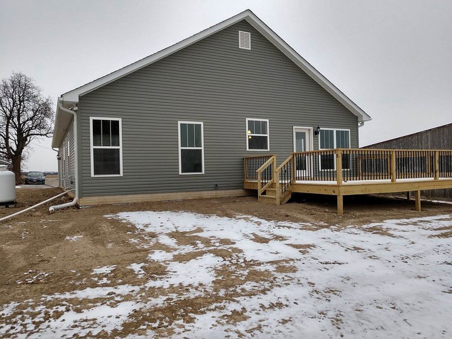 Two-story home with light siding, wooden deck featuring black metal railings, white-framed windows, fenced yard, stairs leading to the deck, snow covering the ground, and a parked