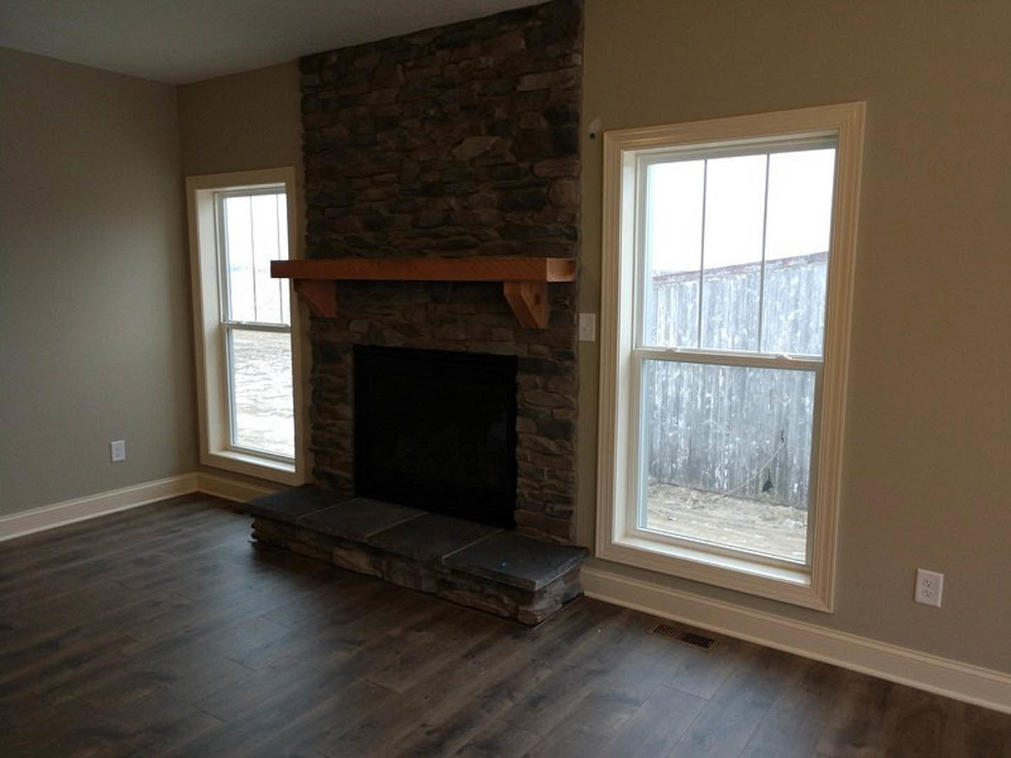 Stone fireplace with black hearth set against a dark wall, wood flooring, large window overlooking ocean, wooden fence visible outside, electrical outlet near stone step.