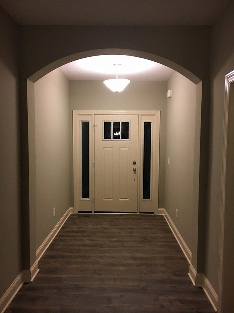 Hallway with dark wood flooring, white baseboards, white door featuring a window, ceiling-mounted light fixture, and smooth plaster walls