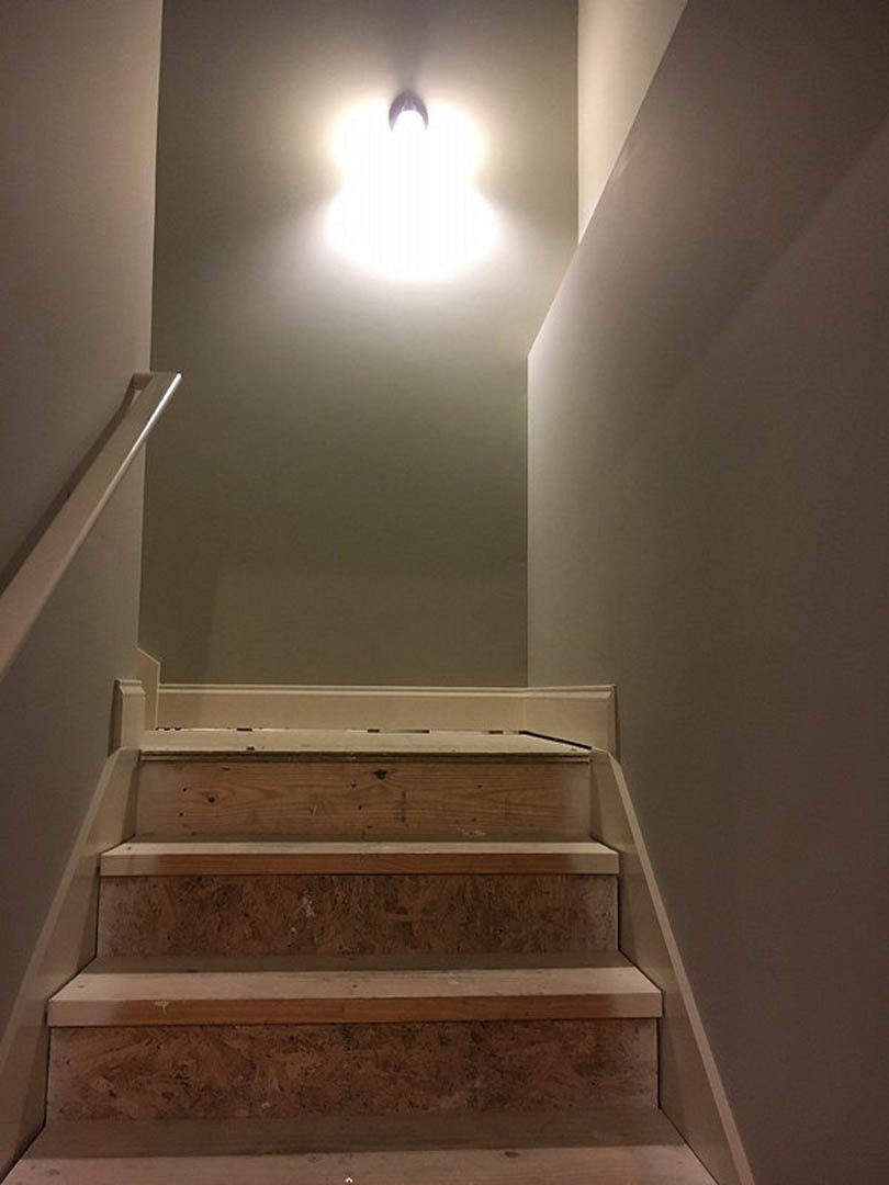 Modern pendant light hangs above wood staircase with white plaster walls and minimalist handrail.