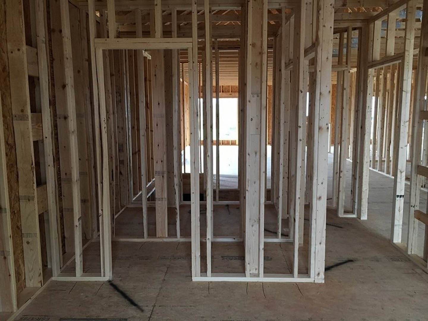 Exposed wood framing and beams in an unfinished room, with visible lumber, floor, and construction materials