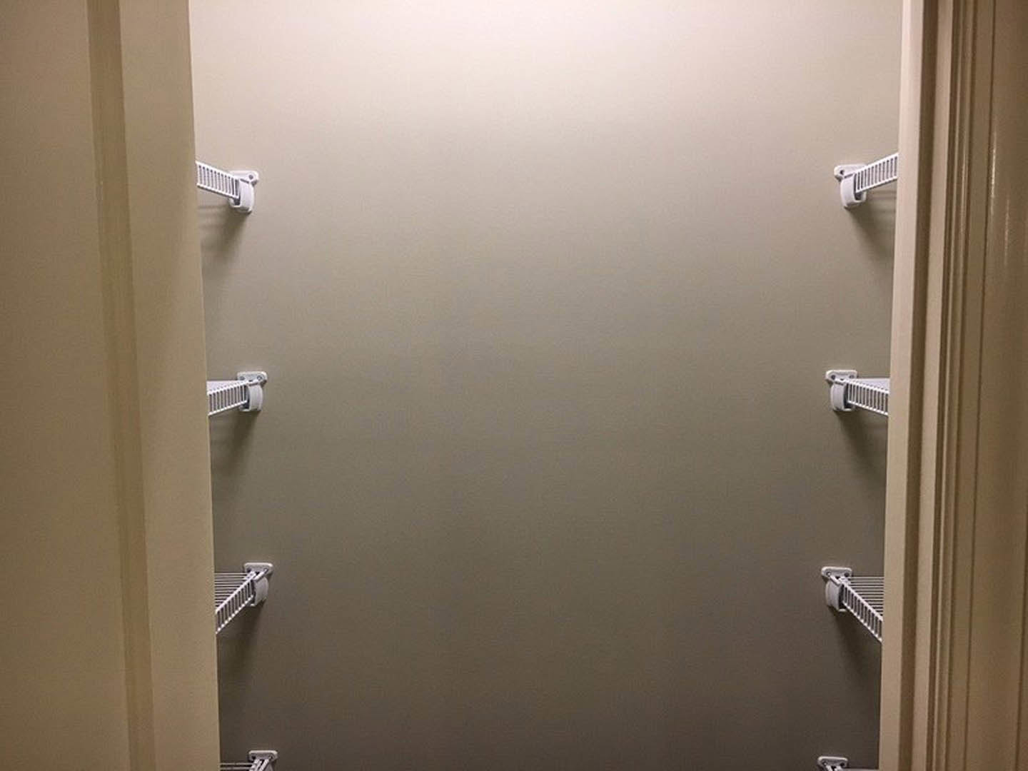 White built-in shelves with a hanging rod mounted on a wall in a closet, featuring smooth white finishes and minimalist design.