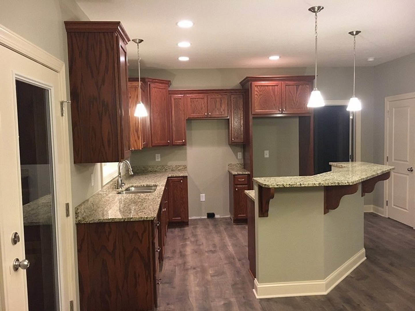 Granite countertops, white tile backsplash, wood cabinetry, stainless steel sink, and recessed lighting in a modern kitchen