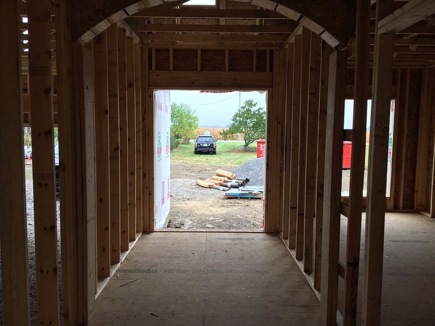 Hallway with light wood flooring and wall, window framing view of black car parked outside near grassy area and tree