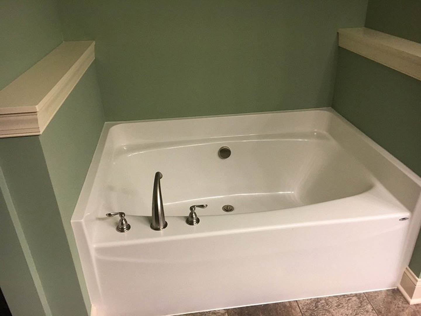 Freestanding white bathtub with chrome faucet set against light tiled bathroom wall