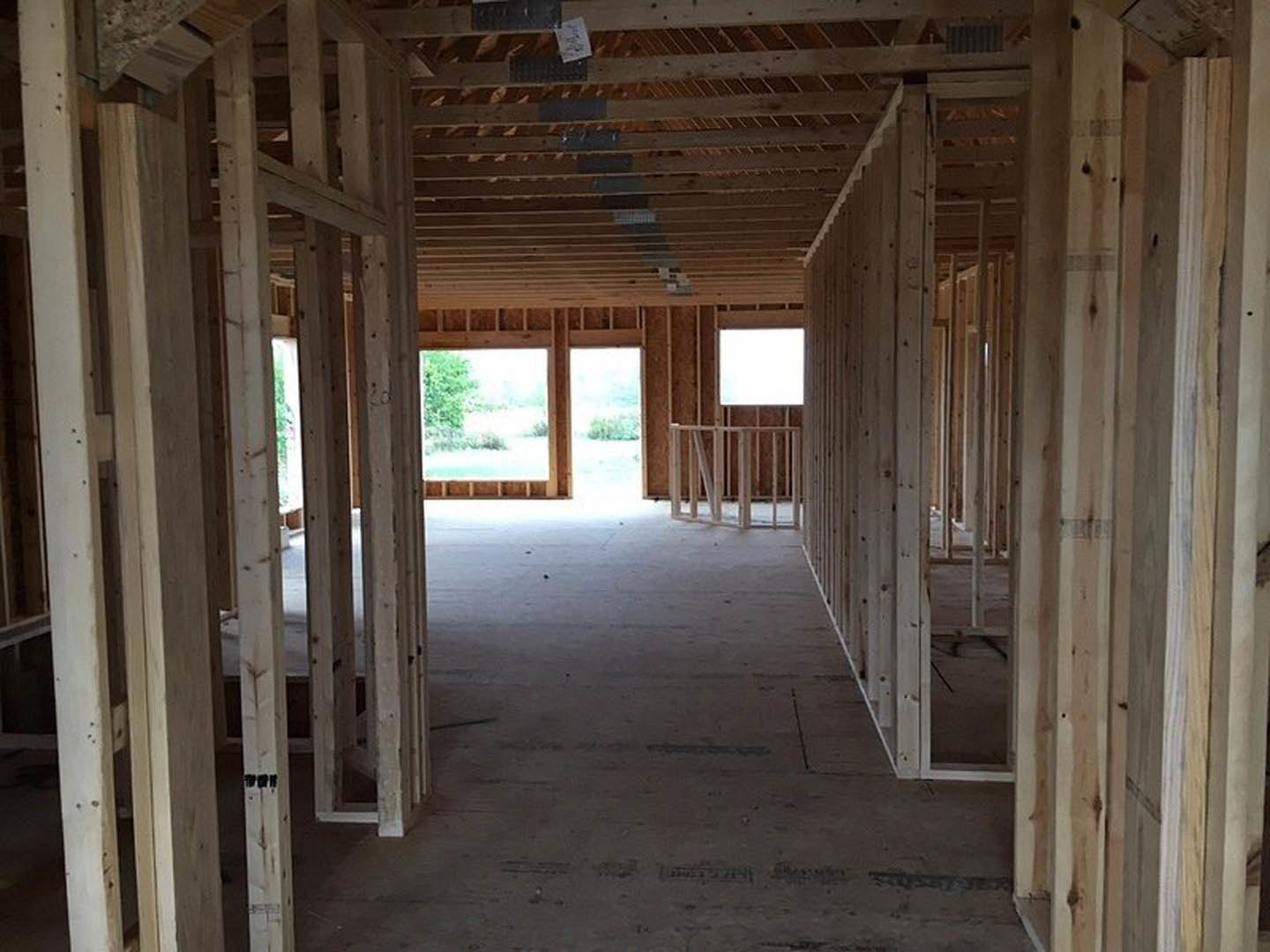Exposed wood framing and beams inside a partially constructed room, window overlooking trees, white paper with black writing resting on a plank, close-up of wooden railing