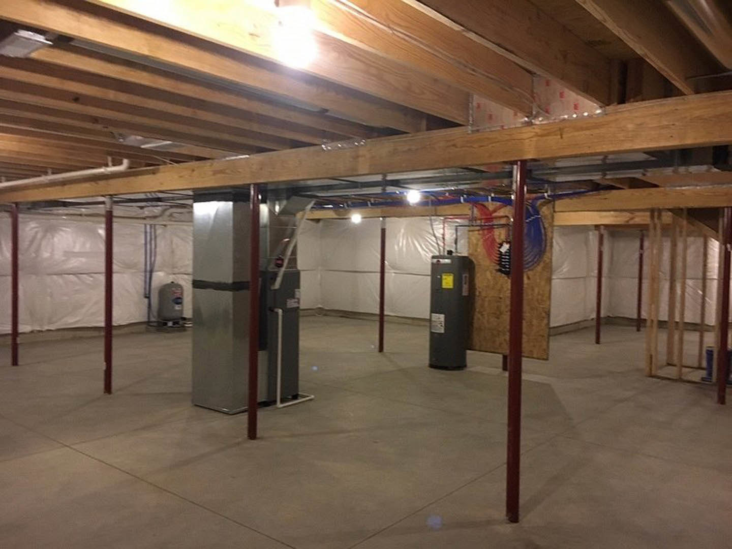 Spacious basement with grey concrete floor, white walls, exposed ceiling beams, and large rectangular metal utility box with yellow label