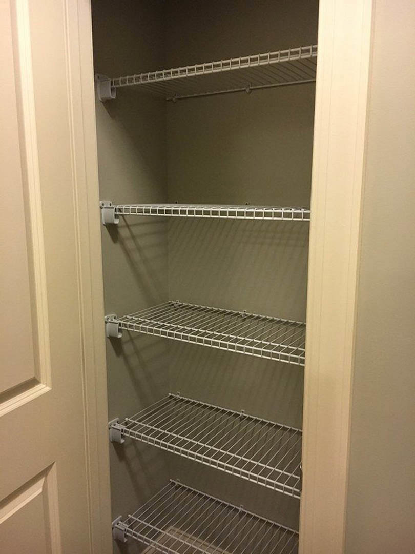 Walk-in closet with built-in white metal shelving and perforated racks, surrounded by light-colored walls and a door.