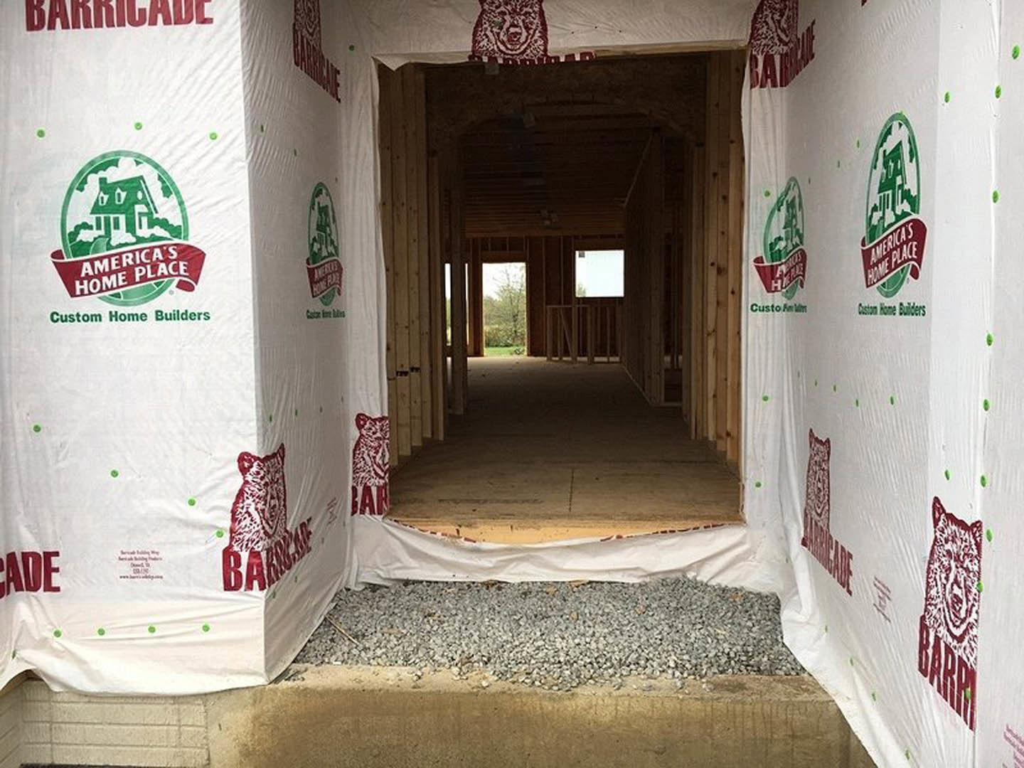 Unfinished hallway with white construction sheets covering walls, window overlooking trees, large white box with green and red logos, close-up of label, exposed floors and doorways