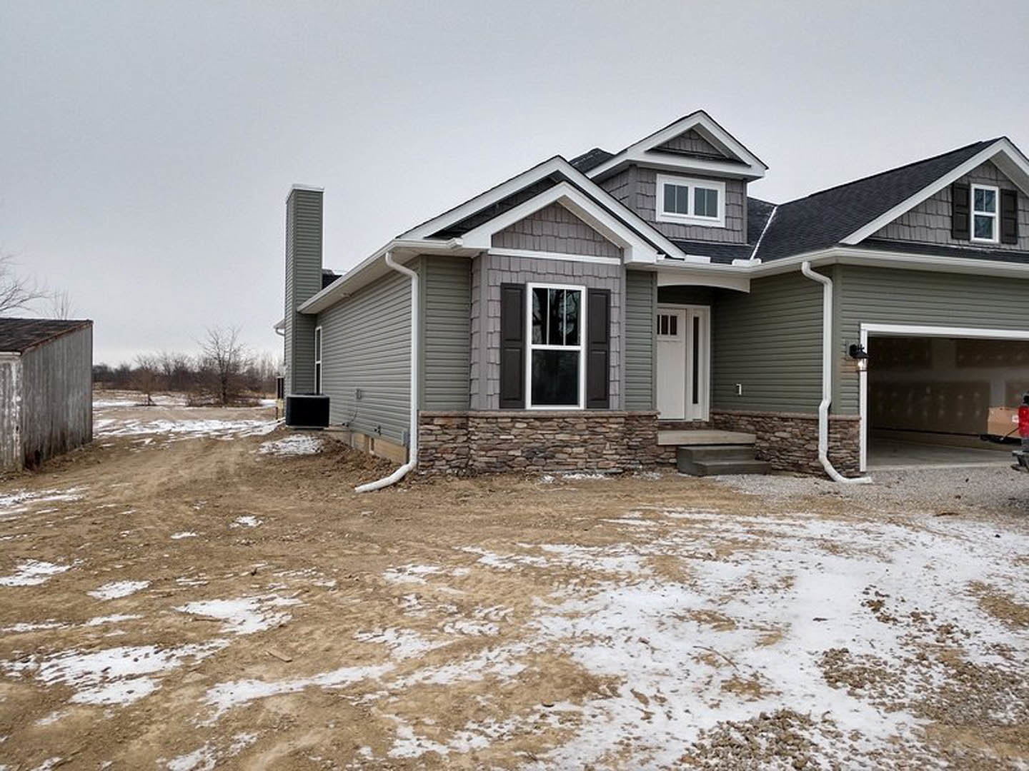 White cottage-style home with white-framed windows, white door featuring glass panel, and snow covering the ground; light-colored siding and black square outdoor fixture visible.