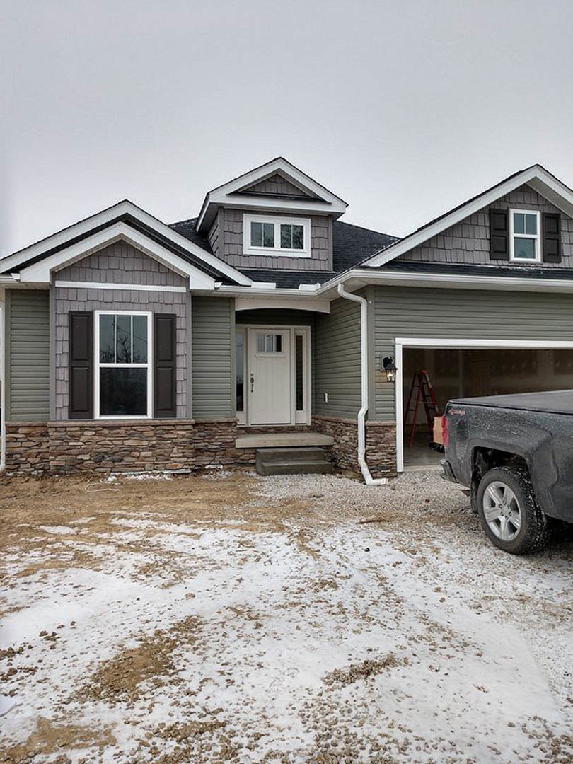 Modern home exterior with white front door and window, black pickup truck parked on snowy driveway, red and black ladder leaning against house, close-up of truck tire visible