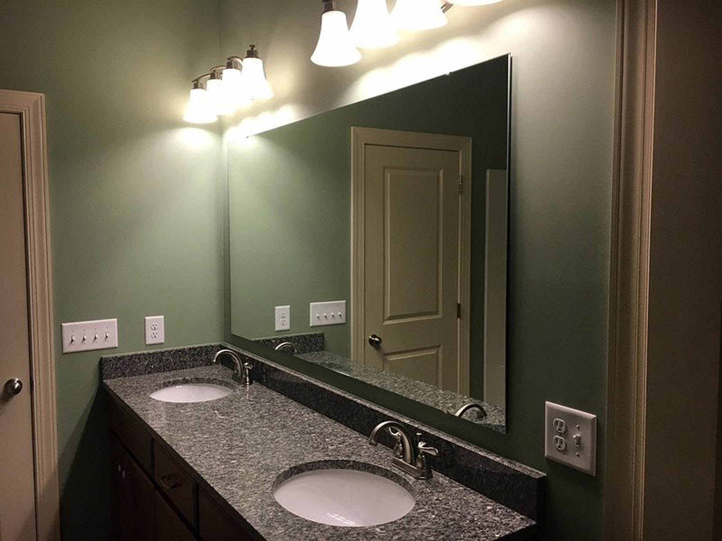 Modern bathroom featuring a wide frameless mirror above a white countertop with an undermount sink, chrome faucet, and wall-mounted switches and outlets on a tiled backsplash