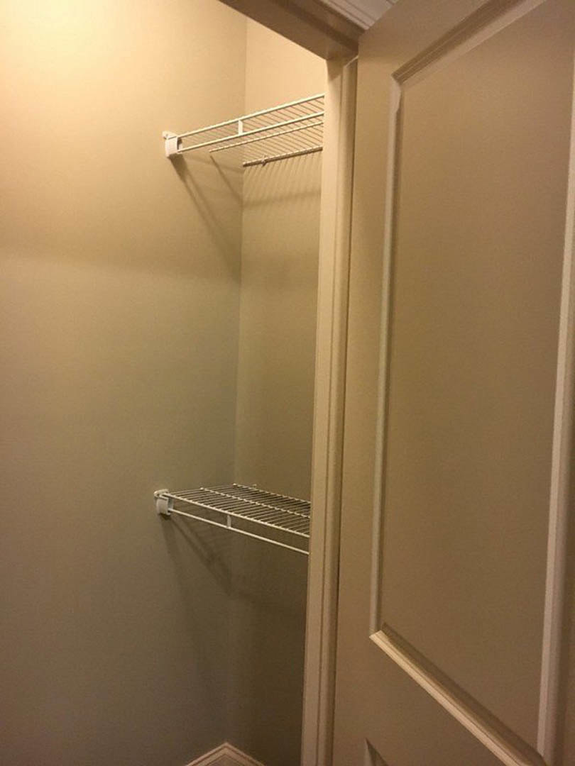 Walk-in closet with built-in white shelves, metal rack with handle, white walls and ceiling, white metal railing along the wall, corner shelving unit