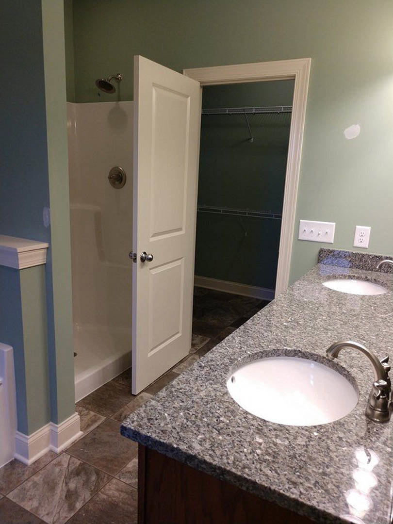 Marble countertop with oval white sink, chrome faucet, glass-enclosed shower, white cabinetry, and tiled walls in a modern bathroom
