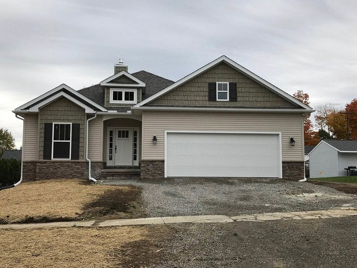 White siding house with attached garage featuring white paneled garage door, white framed windows, glass paneled entry door, brick chimney, and outdoor grill on driveway.