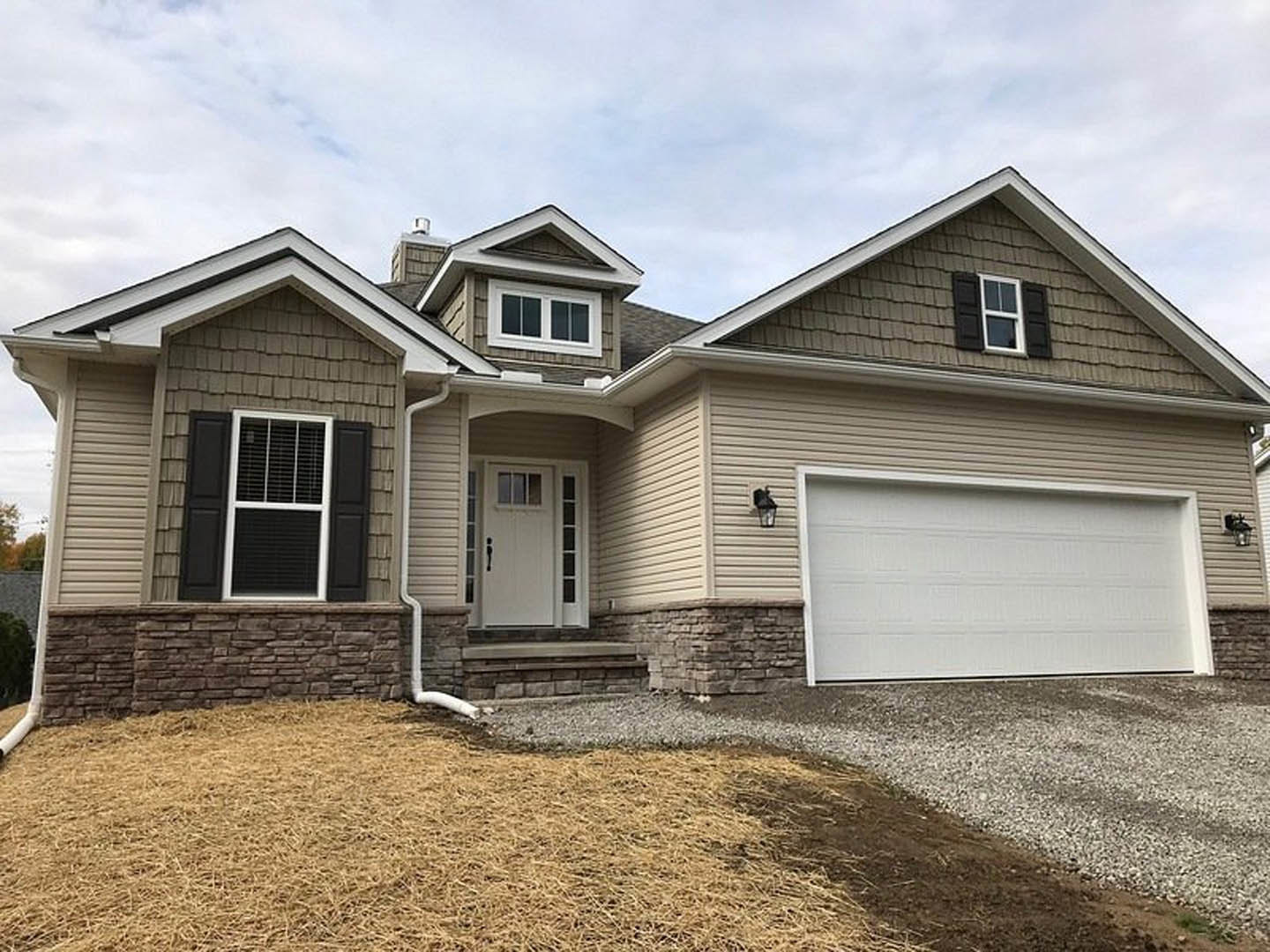 Gray siding house with attached garage, white paneled garage door, black window shutters, white entry door with black handle, manicured lawn, partly cloudy sky
