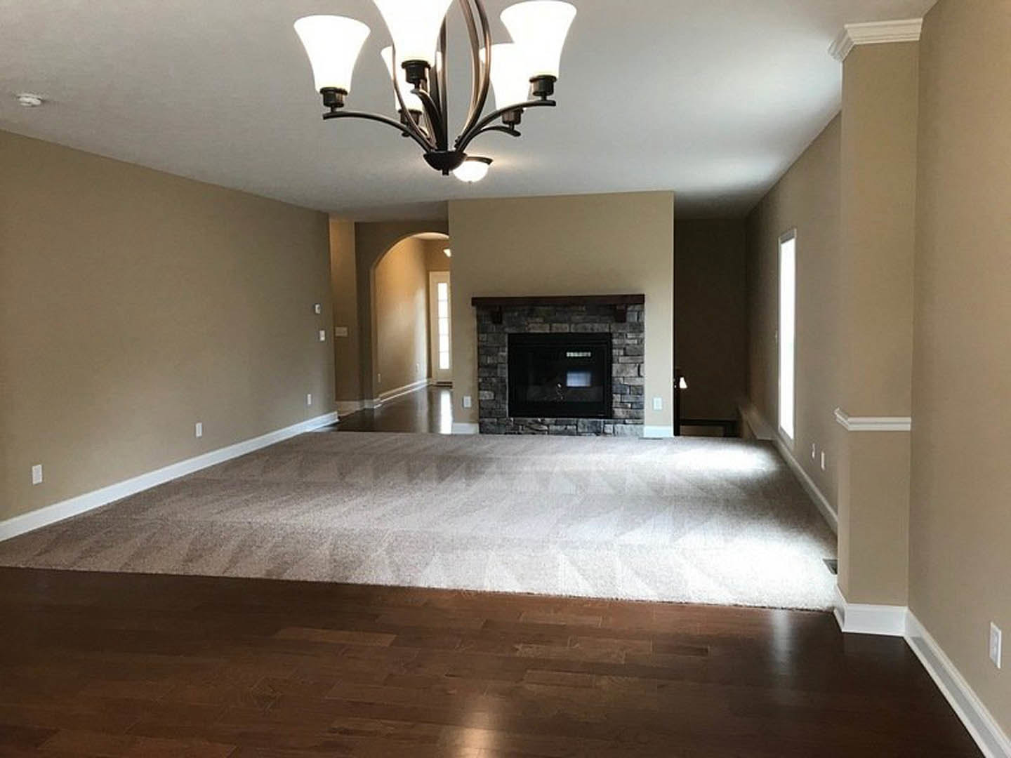 Living room with light hardwood floors, white walls, black-framed fireplace, decorative ceiling molding, and a modern chandelier