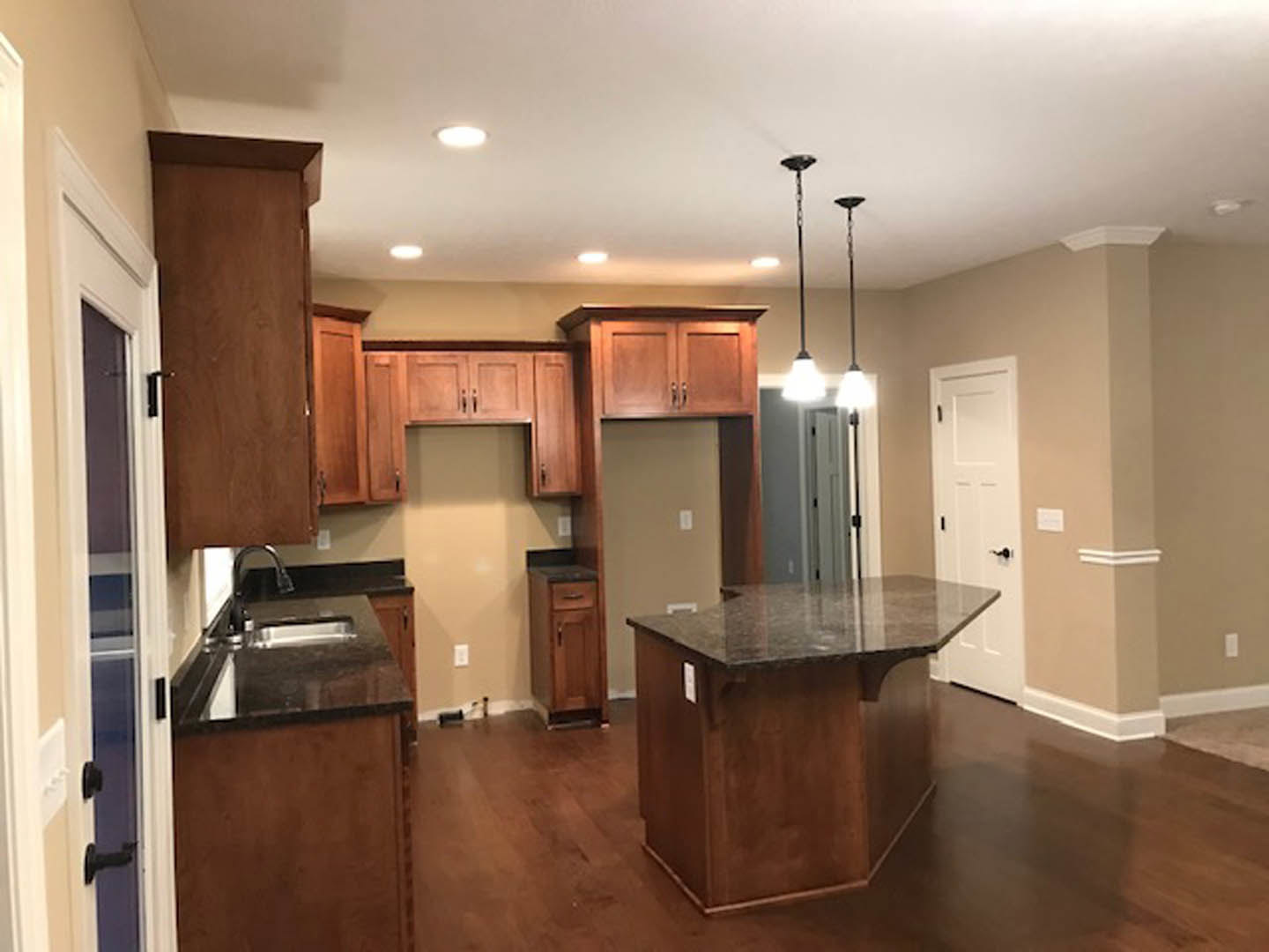 Open kitchen with white shaker cabinets, marble island countertop, stainless steel appliances, light wood flooring, black hardware on doors and drawers, pendant light fixtures