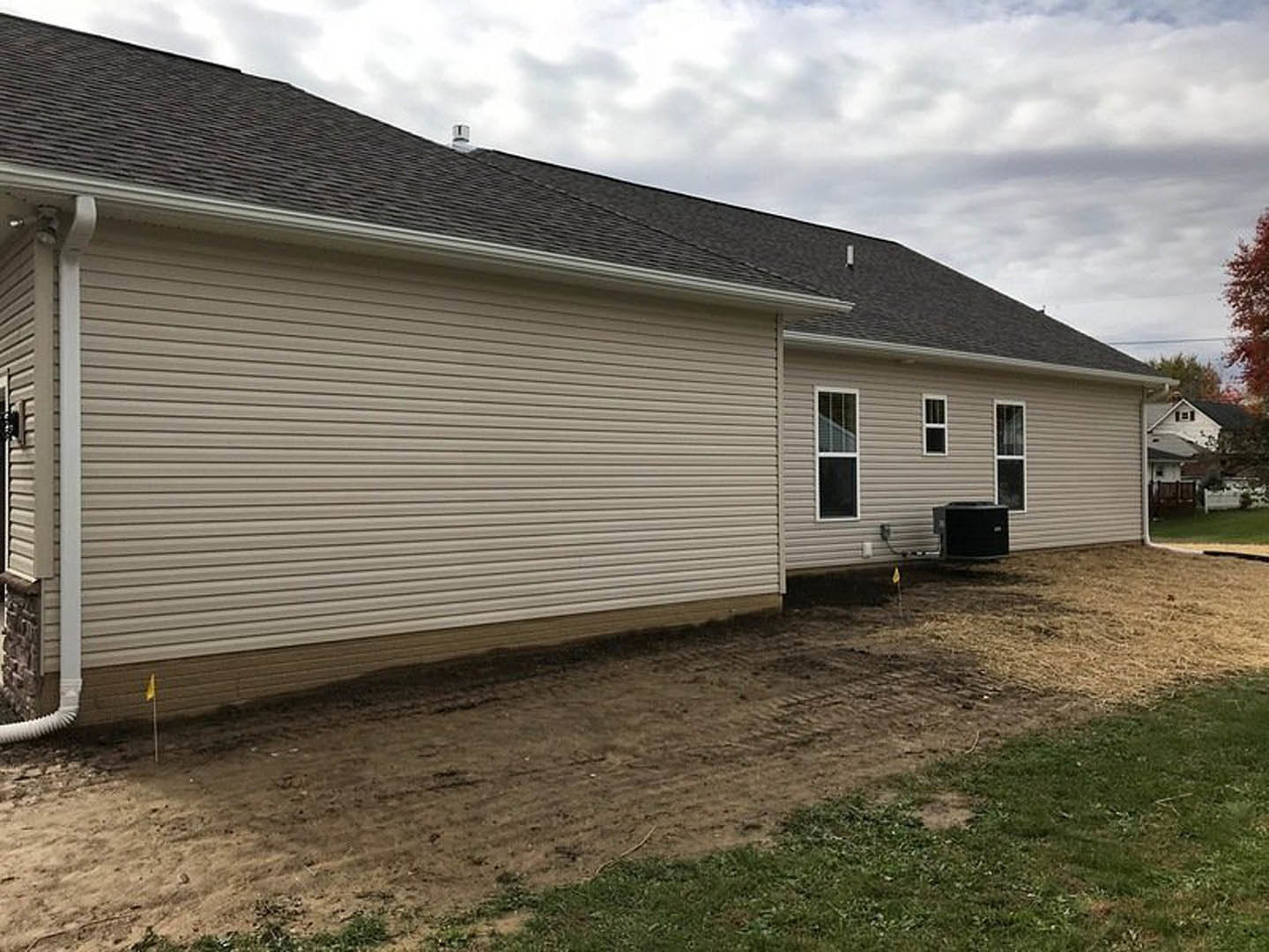Modern home exterior with light-colored siding, white-framed windows, black mailbox with white label, dirt yard with patches of grass, and a gabled roof under a cloudy sky