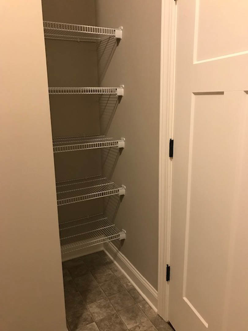 Walk-in closet with white shelves, brown tile flooring, white baseboards, and a white door against smooth white walls