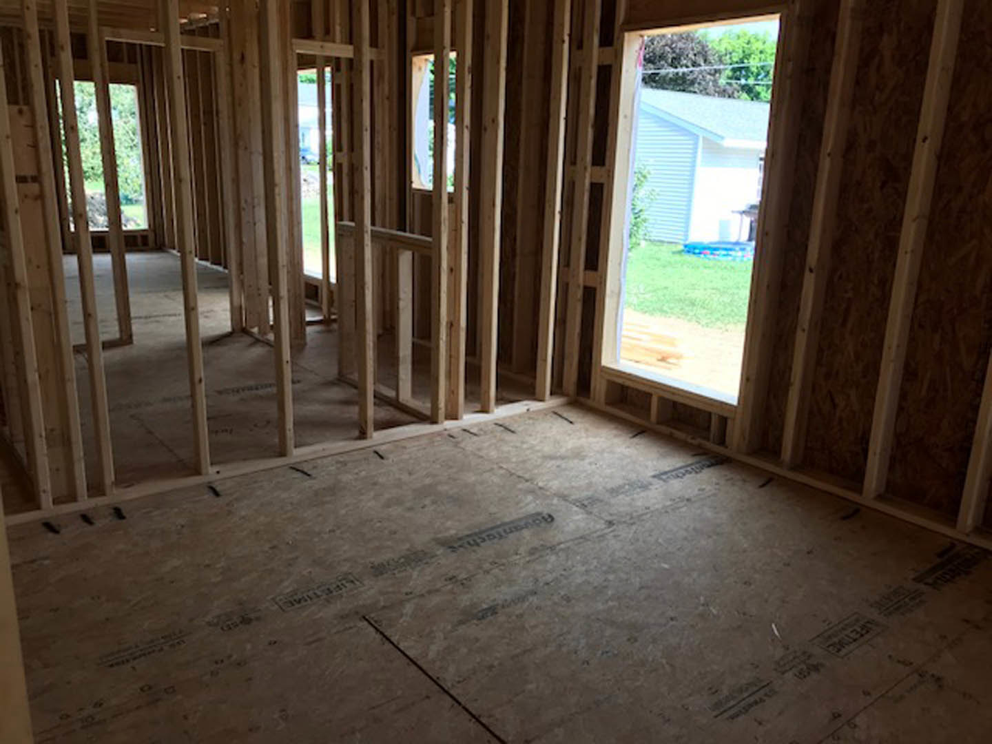 Room under construction with exposed wood framing, unfinished plank flooring, and a window letting in natural light