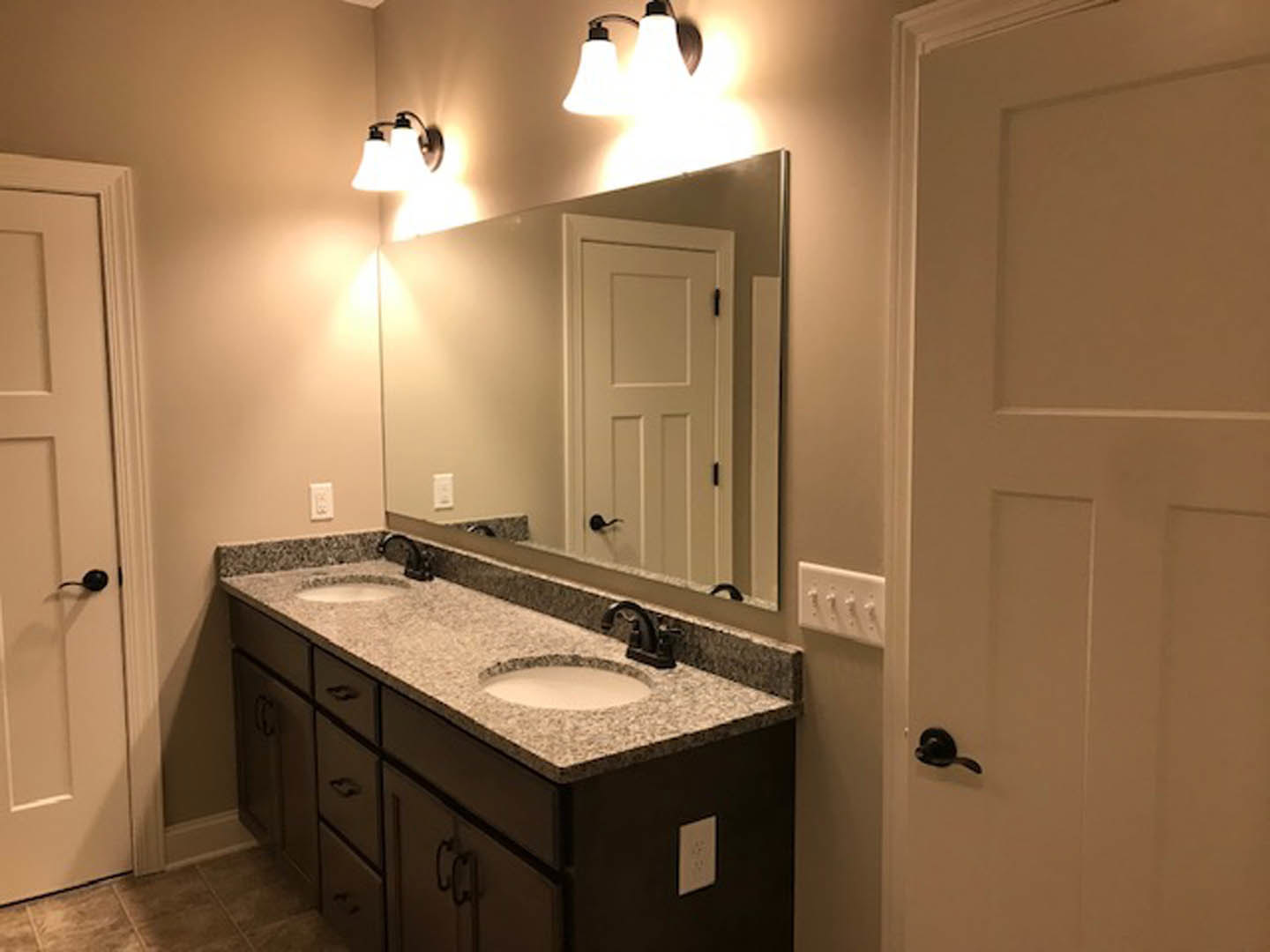 Bathroom with double vanity featuring white countertops with black borders, large wall mirror, modern cabinetry, chrome faucets, and tiled walls.
