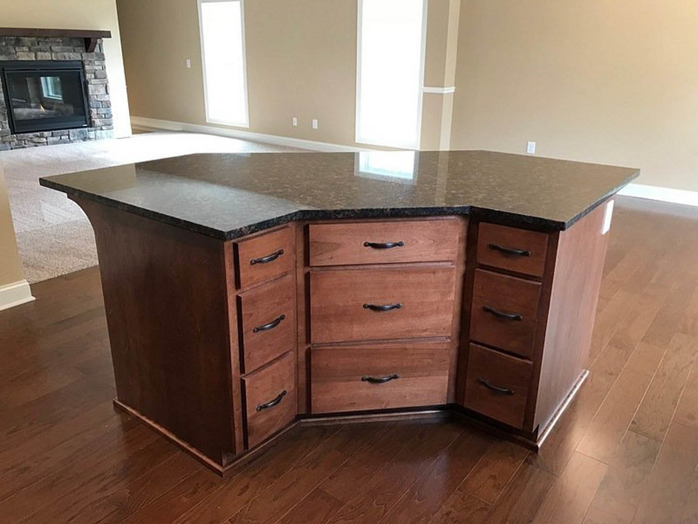 White kitchen island with shaker-style drawers, light stone countertop, brick fireplace wall in background, hardwood flooring
