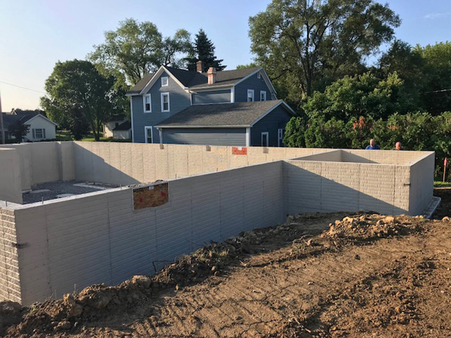 Partially built house with exposed framing, attached garage, dirt construction site, and mature trees in the background